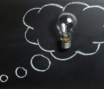 Clear light bulb placed against a blackboard, surrounded by a chalk-drawn thought bubble, symbolising a creative idea or inspiration.