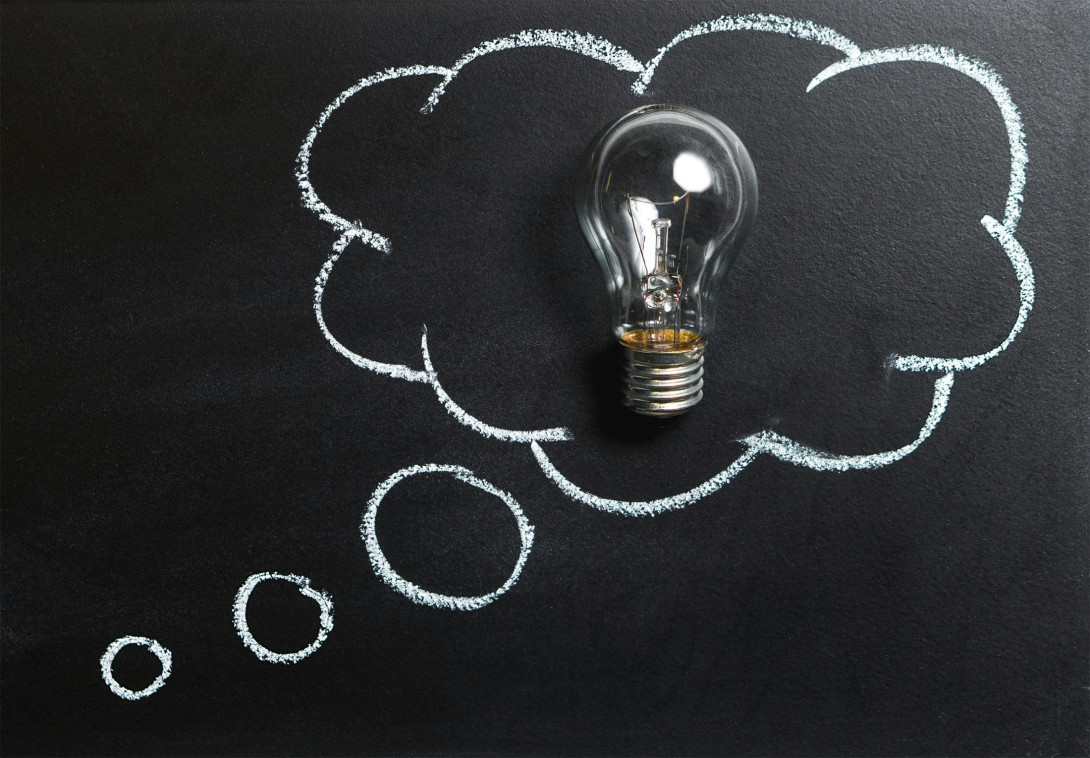 Clear light bulb placed against a blackboard, surrounded by a chalk-drawn thought bubble, symbolising a creative idea or inspiration.
